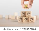 Brainstorming, creative idea or innovative idea concept. Wooden blocks with gear head icon arranged in pyramid stair shape and a man is holding the top one with light bulb icon.