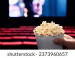 Small photo of Movies and popcorn. Man holding pop corn box at cinema. Action, thriller or scifi entertainment on screen. Red seats in dark theater. Salty snack in bucket. Spectator pov. Film premiere.