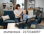 Small photo of I am the winner. Mother and her agreeable elated pretty little girl giving high five after playing piano at music room. Musician lesson concept.