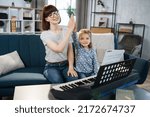 Small photo of I am the winner. Mother and her agreeable elated pretty little girl giving high five after playing piano at music room. Musician lesson concept.