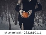 Beautiful faceless woman in black tight dress with a pumpkin in hands in the dark forest, selective focus. Halloween, gothic, witch, November, magic vibes, authentic, athmospheric, dark beauty concept