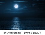 This large full blue moon rises brightly over the cloud bank in this calm ocean creating sparkles accross the waves in this beautiful tranquil scene. 