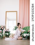 Small photo of Beautiful woman in white underwear and negligee at home in the room among flowers of roses and tulips.. A woman in love is resting and prepare for wedding day.