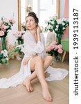 Small photo of Beautiful woman in white underwear and negligee at home in the room among flowers of roses and tulips.. A woman in love is resting and prepare for wedding day.