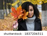 Portrait of a smiling young African American woman with autumn maple leaves in the park.