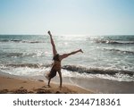 The young woman does gymnastics and acrobatics on the beach. Woman in a bathing suit enjoys her vacation on the beach, at sea.
