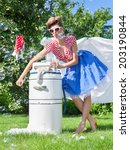 Small photo of Pin up style photo of woman doing laundry using vintage wringer washing machine