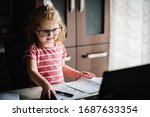 Smart little toddler girl wearing big glasses while using her laptop at home. Young beautiful girl sitting at working place in office.
