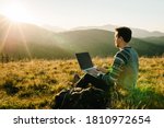 Man working outdoors with laptop sitting in mountains. Concept of remote work or freelancer lifestyle. Cellular network broadband coverage. internet 5G. Hiker tourist enjoying valley view sunset.