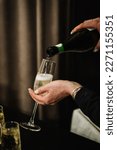 Small photo of Woman pours champagne into a flute glass. Champaign is being pored into glasses. Waiter pouring white sparkling wine. Bottle in a closeup view. Catering service concept.
