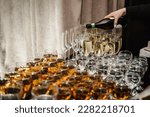 Catering service concept. Woman pours champagne into flute glasses. Champaign is being pored into glasses. The waiter pouring white sparkling wine. Bottle in a closeup view. Rows of full glasses.