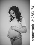 Small photo of Female waiting for newborn baby on white background. Young pregnant girl holding belly and caring about health. Pregnancy motherhood procreation concept. Belly of pregnant woman. Black and white photo