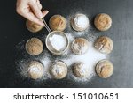 Woman's hand sprinkling icing sugar over fresh muffins.