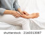 Small photo of Dry feet, cracked soles with scales, dermatitis, peeling, eczema, psoriasis and xerosis and skin care concept. A woman touches her unhealthy leg while sitting on the bed at home.