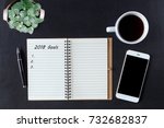 Flat lay of notebook with action 2018 goals and smartphone, on black office desk. Office desk on top view.