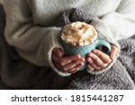 Small photo of Woman with blanket warming her hands in mug of hot drink with whipped cream