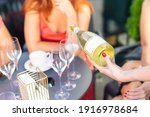 Close-up female waiter holding bottle of white champagne or prosecco at outdoor party on bright summer day. Girls hen-party concept. Luxury life lifestyle. refreshing light alcoholic beverages