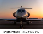 Scenic front view modern luxury expensive private jet plane parked airport taxiway hangar warm colorful dramatic evening warm sunset sun light sky background. Executive aicraft vip travel concept