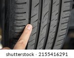 Small photo of Mechanic pointing with hand at tyre wear indicator at car service center. Vehicle wheel protector control and inspection during maintenance. Tread wear check test inspection at automotive maintenance