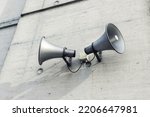 Small photo of Pair of big retro loudspeakers mounted on grey concrete cement wall. Air raid nuclear strike alert speaker siren. Urgent or emergency announcement, message event. Dictatorship regime concept