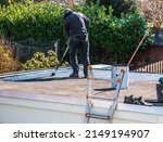 Small photo of Roofer rolls a tar sheet with bitumen on a flat roof