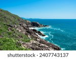 Small photo of The picture shows a rocky coastline with turquoise-green water, green slopes and an absolutely blue sky without clouds.