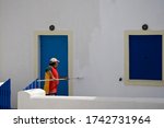 Greek man in red shirt painting a white wall of a traditional building in Santorini, preparing for first tourists