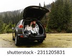 a couple in love sits in the trunk of a car. travel by car in the mountains and near the river. autumn journey during the rain. picnic in the car