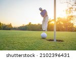 Small photo of Blurred Golfer putting ball on the green golf, lens flare on sun set evening time. Golfer action to win after long putting golf ball in to the hole.