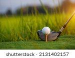 Small photo of Golf club and ball on green grass ready to be struck on golf course background, Lens flare on sun set evening time. Golf ball on tee in front of driver on a golf course.
