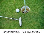 Small photo of Top view of a golf ball with putter on green course at hole. Golf ball and golf club on green in the evening golf course with sunshine.
