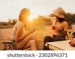 Wonderful evening moment : Two asian female friends sitting and chatting cheerfully drinking freshly brewed coffee watching the beauty of nature mountain forest and sunset on vacation trip.