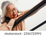 Small photo of Asian elderly woman in frail health sick with acute heart disease walking up the stairs of the house shortness breath dizziness headache hand touches the railing to prevent danger or fall downstairs.