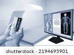 Small photo of Close-up Doctor uses a smartphone to check an Image of a DXA bone density scan on a monitor in a woman to prevent osteoporosis. blurry bone densitometer machine background.Medical technology concept.