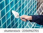 Small photo of Male hand construction worker using trowel or building spatula spreading cement grout on blue ceramic tiles in the swimming pool