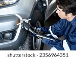 Small photo of Car insurance claim process. Asian male car insurance agent or auto mechanic man using digital tablet and pen checking car scratch abrasion on front bumper