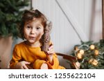 Cute curly toddler girl wearing mustard linen dress in studio near christmas tree with chocolate St Nicholas. Minimalistic stylish scandinavian christamas decoration.