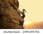 Beautiful Woman Climbing on the High Rock at Foggy Sunset in the Mountains. Adventure and Extreme Sport Concept