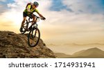 Cyclist Riding the Bike Down the Rock at Sunrise in the Beautiful Mountains on the Background. Extreme Sport and Enduro Biking Concept.