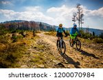 Mountain biking woman and man riding on bikes at sunset mountains forest landscape. Couple cycling MTB enduro flow trail track. Outdoor sport activity.