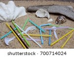 Pollution of plastic straws and fork left on beach background with beautiful seashells and drift wood.  Plastic pollution is harmful to  marine lives. Environmental concept. Ban single use plastic. 