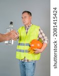 Small photo of A male construction worker in work clothes refuses a proffered bottle of strong alcohol