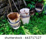 Small photo of A stack of old rusty iron inapplicable buckets against a background of green grass in an abandoned farmyard yard