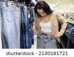 Young woman shopaholic choosing jeans in luxury store, woman try on pants on big sale in shop