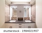 Small photo of Alcove double vanity sink with wood panel walls and cabinet. Stylish vanity unit with two mirrors with wooden white frame with built in cabinet in the middle above the granite countertop.