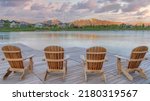 Panorama Puffy clouds at sunset Four wooden lounge chairs facing the reflective Oquirrh Lake at Daybreak, Utah. Wooden dock with a view of the residential area against the mountain range background.
