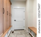 Small photo of Square Mudroom interior with white fire door and a flooring with herringbone pattern. There is a seat with shoe storage underneath on the left and a wooden cabinet with a storage at the bottom.