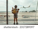 Child, watching from the window of the airport the planes, taking off and landing while waiting at  to board the aircraft for a holiday