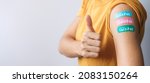 Small photo of Happy woman showing Thumb sign with bandage after receiving covid 19 vaccine. Vaccination, herd immunity, side effect, booster dose, vaccine passport and Coronavirus pandemic