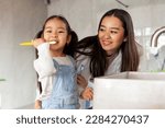 asian little girl with mom brushing teeth in bathroom, korean woman helping to brush daughter's teeth at home together, asian family and hygiene procedures